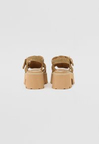 Sandali platform intrecciati marroni con suola chunky, cinturino alla caviglia regolabile e dettagli testurizzati sulla parte superiore.