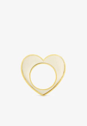 Anillo en forma de corazón con contorno dorado y relleno de esmalte color crema, con un recorte circular en el centro.