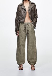 Bruine leren cropped bikerjas met zilverkleurige hardware, gecombineerd met losse olijfgroene broek met een elastische tailleband en trekkoord.