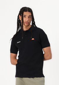Melns polo krekls, kas izgatavots no kokvilnas, ar apkakli, īsām piedurknēm un izšūtu oranžu un sarkanu logo kreisajā krūtī.