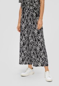 Schwarz-weiße, mit Paisleymuster versehene, weit geschnittene Hosen mit strukturierter Oberfläche, kombiniert mit weißen Turnschuhen. Der Bund ist elastisch für zusätzlichen Komfort.