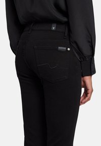 Jeans de denim negro con un estilo ajustado, que cuentan con bolsillos traseros, una etiqueta cerca de la cinturilla y detalles de costura sutiles.