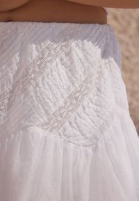 Tissu blanc texturé avec des détails de smocks et une incrustation de dentelle. Design évasé, finition douce et motifs variés créent un intérêt visuel.