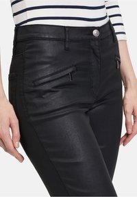 Černé kalhoty z umělé kůže s hladkým povrchem, se dvěma předními kapsami, stříbrnými detaily a sníženým střihem.
