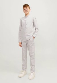 Helehall, pikad varrukad, mandariinkaelusega ja nööpidega särk, mida kannab kokku sobivad helehallid püksid ja valged tennised.