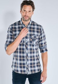 Karierte Hemd in Blau, Braun und Weiß. Lange Ärmel hochgekrempelt. Verfügt über zwei Brusttaschen und einen Knopfkragen.