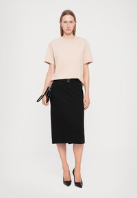 Light pink oversized t-shirt, black pencil skirt with a shiny black belt, and black pointed toe heels, posing against a white background.