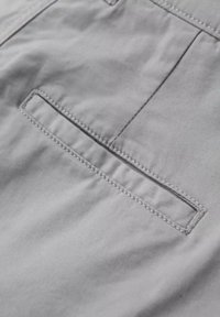 Gros plan sur un tissu gris clair avec une poche fendue horizontale présentant des coutures soignées le long des bords.