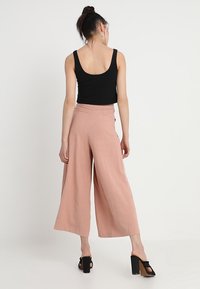 Pale pink wide-leg trousers with a high waist and a smooth texture, paired with a black sleeveless top and black platform heels.