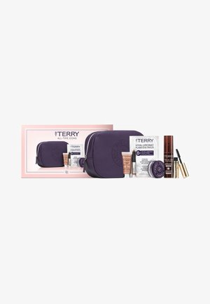 Lila Lederkosmetiktasche mit geprägt Logo, begleitet von Hautpflege- und Make-up-Produkten in verschiedenen Behältern, vor einem pinken Kasten.