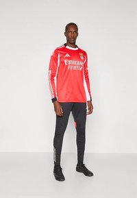 Dlhý červený dres s bielymi akcentmi, s logom "Emirates". Kombinovaný s priliehavými čiernymi nohavicami s tromi zlatými pruhmi na bokoch a čiernymi topánkami.