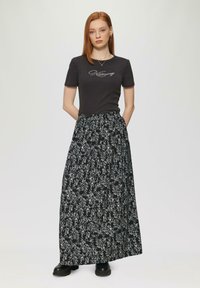 Schwarzer Maxi-Rock mit flotten weißen Mustern, kombiniert mit einem eng anliegenden grauen T-Shirt mit geschwungenem Text. Der Rock hat einen elastischen Bund.