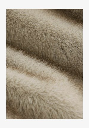 Puha bézs színű műszőrme anyag, változó textúrákkal, hosszú, finom szálakkal, amelyek puha, tapintásra kellemes felületet alkotnak.