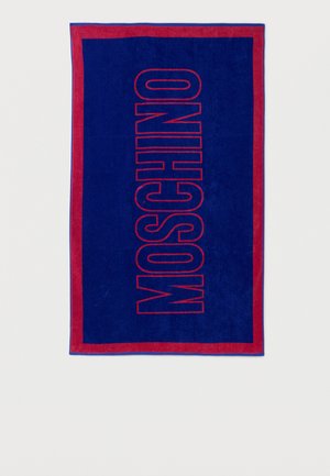 Serviette rectangulaire bleu marine avec bordure rouge et grand texte vertical "MOSCHINO" en contours rouges centré.