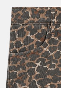 Denimová tkanina s leopardím vzorom, ktorá sa vyznačuje kombináciou hnedých, béžových a čiernych farieb. Obsahuje prednú vrecko a kontrastné stehy.