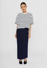 Stripet hvid og navy cropped t-shirt med løs pasform, parret med en navy ribbet maxiskirt, afsluttet med en bølget kant, båret med sorte flade sko.
