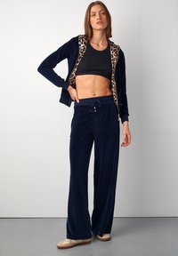 Námořnický sametový teplákový komplet s kapucí podšitou leopardím vzorem, zipem na přední straně, černým crop topem, širokými kalhotami a béžovými nazouvacími botami.