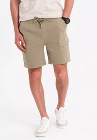 Shorts cargo beiges avec une taille élastique et un cordon de serrage, comportant des poches latérales et une coupe décontractée. Portés avec un t-shirt de couleur claire et des baskets.