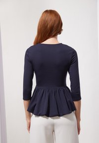 Tumed peplum-top, millekolmnurga varrukatega, liibuv kehaosa ja pehme, tekstureeritud kangas; pleeditud vöökoht lisab volüümi.