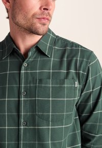 Green plaid button-up shirt made of soft fabric, featuring a chest pocket, classic collar, and contrasting white grid pattern.