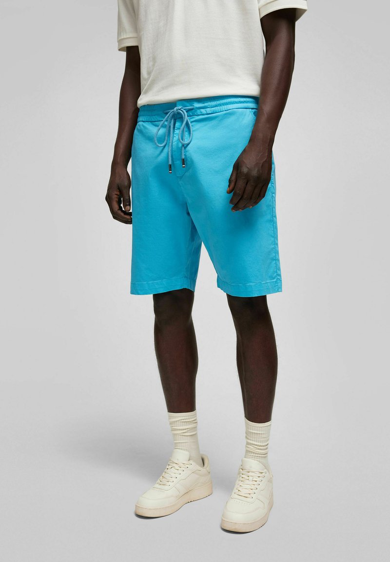 Lichtblauwe korte broek met een elastische tailleband en een trekkoord. Heeft een soepele textuur en een eenvoudig ontwerp, gecombineerd met witte sneakers en sokken.