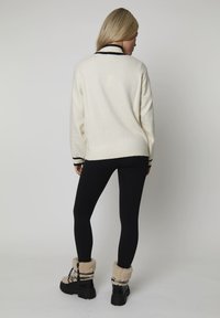 Romige gebreide trui met een geribde kraag, zwarte strepen bij de manchetten, gecombineerd met zwarte leggings en zwarte, met bont gevoerde enkellaarsjes.