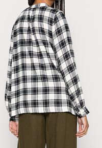 Chemise à boutons à carreaux noirs et blancs, manches longues, avec une coupe ample et un ourlet arrondi, fabriquée en tissu léger.