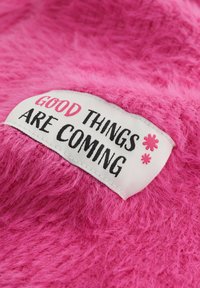 Biała etykieta z różowym i czarnym napisem "Dobre rzeczy nadchodzą" na jasnoróżowym, puszystym tle.