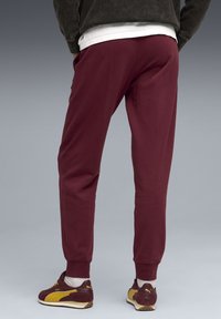 Burgundy sweatpants med en afslappet pasform, med sidelommer og elastiske manchetter. Parret med brune og gule sneakers.