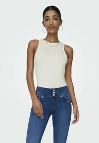 Cremefarvet tanktop kombineret med højtaljede blå denimjeans med knaplukning, forlommer og en glat tekstur.