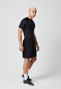 Zwarte sportieve shirt en shorts gemaakt van rekbare stof; het shirt is aansluitend, de shorts hebben een elastische tailleband en zijzakken; gecombineerd met donkere sneakers.