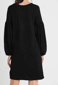 Vestido negro hasta la rodilla con mangas largas y abullonadas y escote redondo. Hecho de una tela suave con una textura lisa. Diseño simple y sólido.