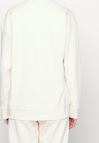 Crèmekleurige katoenen sweat met een relaxte pasvorm, verlaagde schouders en geribbelde boorden. Zachte textuur en eenvoudig ontwerp, zonder zichtbare afbeeldingen.