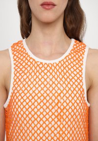 Débardeur en maille orange avec un motif en diamant. Présente un col rond et des emmanchures blancs. Le matériau semble léger avec une finition texturée.