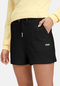Shorts de sport noirs en tissu doux, avec une taille à cordon, des poches latérales et un petit logo blanc et rouge sur la jambe inférieure.