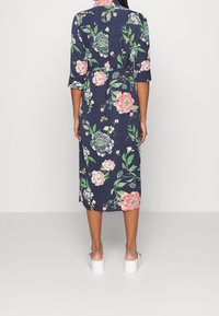 Abito midi a stampa floreale in navy, con vita cinturata, maniche a tre quarti e un tessuto liscio. Il design include fiori rosa e verdi.