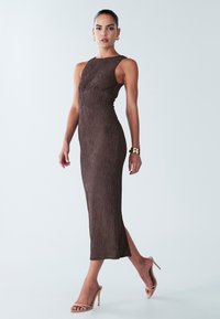 Gaun midi cokelat bertekstur dengan desain tanpa lengan, siluet yang cocok, belahan samping, dan kain bertekstur. Dipasangkan dengan sandal tumit tinggi nude.