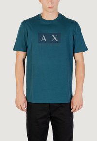 T-shirt en coton teal avec un graphique rectangulaire comportant les lettres "A X" en blanc, et "ARMANI EXCHANGE" imprimé en dessous en texte plus petit.