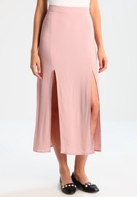 Jupe maxi rose en tissu léger, dotée de fentes latérales doubles et d'une taille lisse. Portée avec des chaussures plates noires.