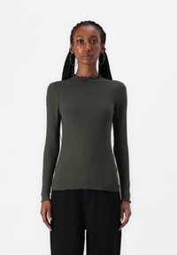 Olive green ribbed long-sleeve top with a high neck and frilled trim. Fitted silhouette, smooth texture, worn with black pants.