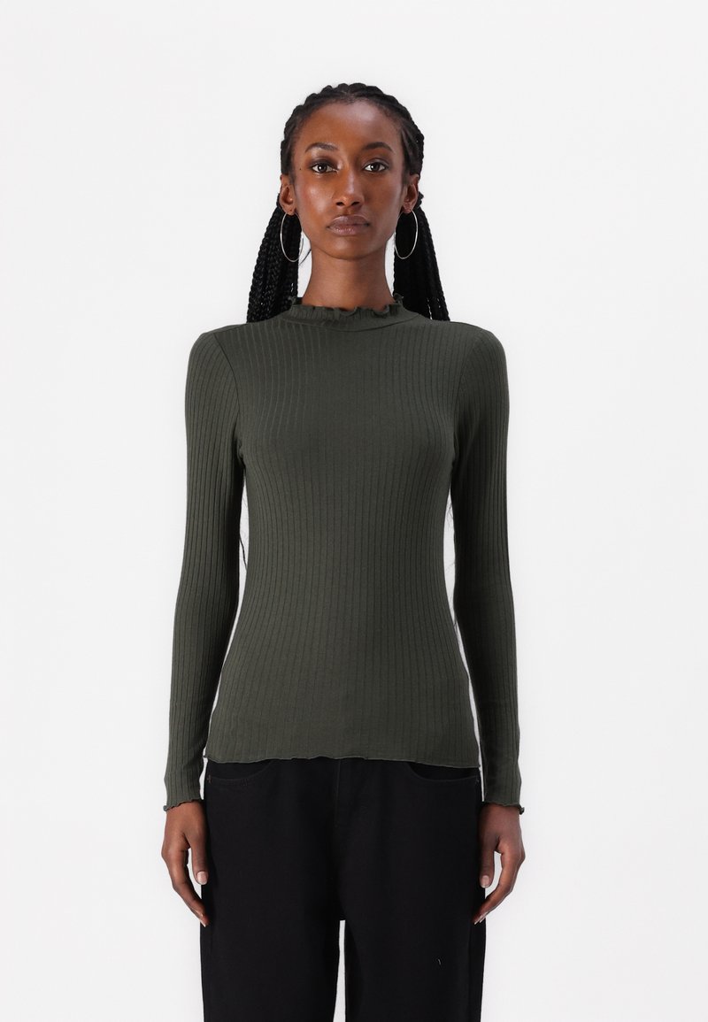 Olive green ribbed long-sleeve top with a high neck and frilled trim. Fitted silhouette, smooth texture, worn with black pants.