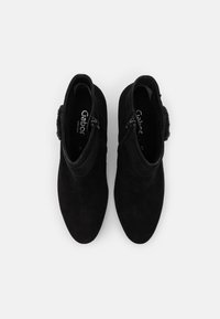 Botas de tobillo de ante negro con una textura suave, que cuentan con una cremallera lateral y adornos decorativos en un lado, diseñadas para la comodidad.