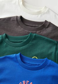 Quatre sweat-shirts à col rond en blanc, gris foncé, vert et bleu. Chacun a un col côtelé et des textures variées, le bleu présentant un design imprimé.