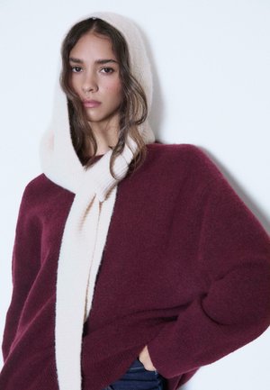 Bordeaux oversized trui met een zachte crèmekleurige sjaal. De trui heeft een relaxte pasvorm; de sjaal is knus en heeft een geribde textuur.