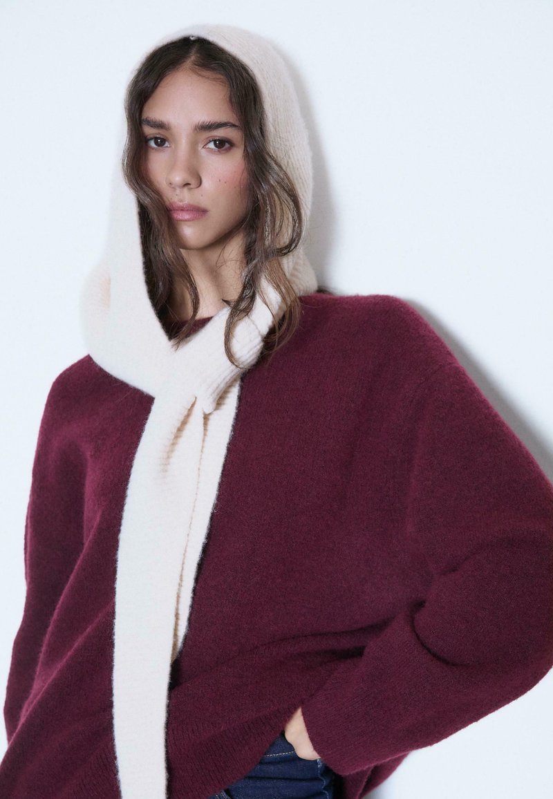Burgundské oversized sveter s mäkkým krémovým šálom. Sveter má uvoľnený strih; šál je príjemný a má rebrovanú štruktúru.