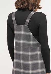 Robe grise à carreaux avec un dos droit, des bretelles réglables et un tissu texturé. Caractérisée par un décolleté carré et un corsage ajusté.