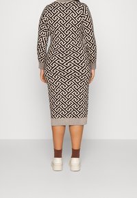 Robe midi en tricot avec un motif géométrique noir et beige, manches longues et poignet côtelé, associée à des baskets blanches et des chaussettes marron.