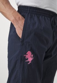Pantaloni corti blu navy con cintura elastica, dotati di un logo di cavallo ricamato in rosa sulla tasca sinistra e tessuto testurizzato.