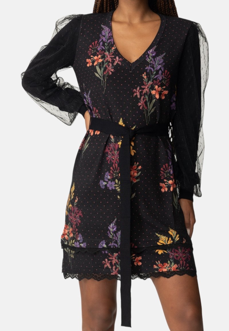 Black floral dress with textured sheer sleeves, V-neck, belted waist, and scalloped hem. Features multicolored flowers against a polka-dot background.