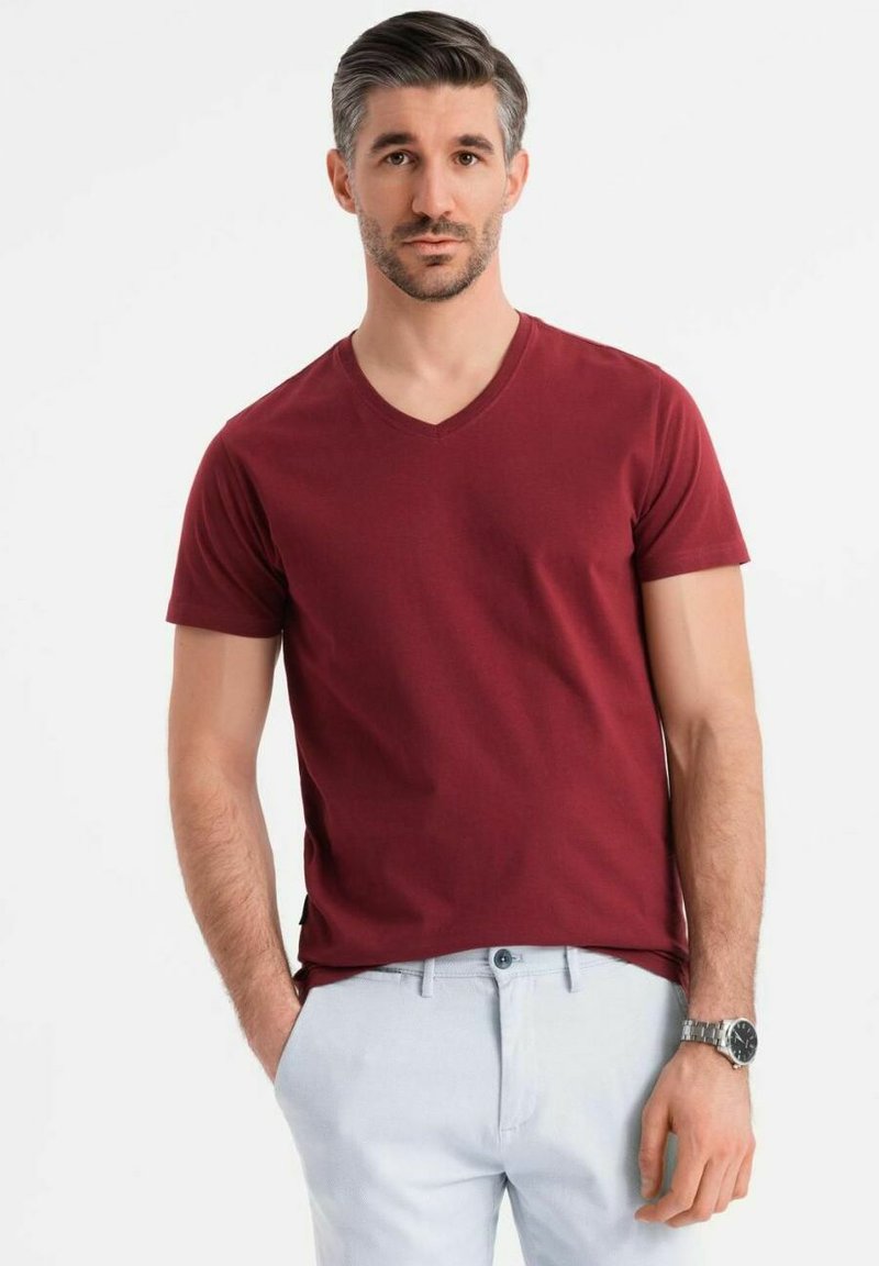 Burgundské tričko s výstřihem do V z jemné bavlny, krátké rukávy, hladká textura, zkombinované se světle modrými kalhotami a stříbrnými hodinkami.